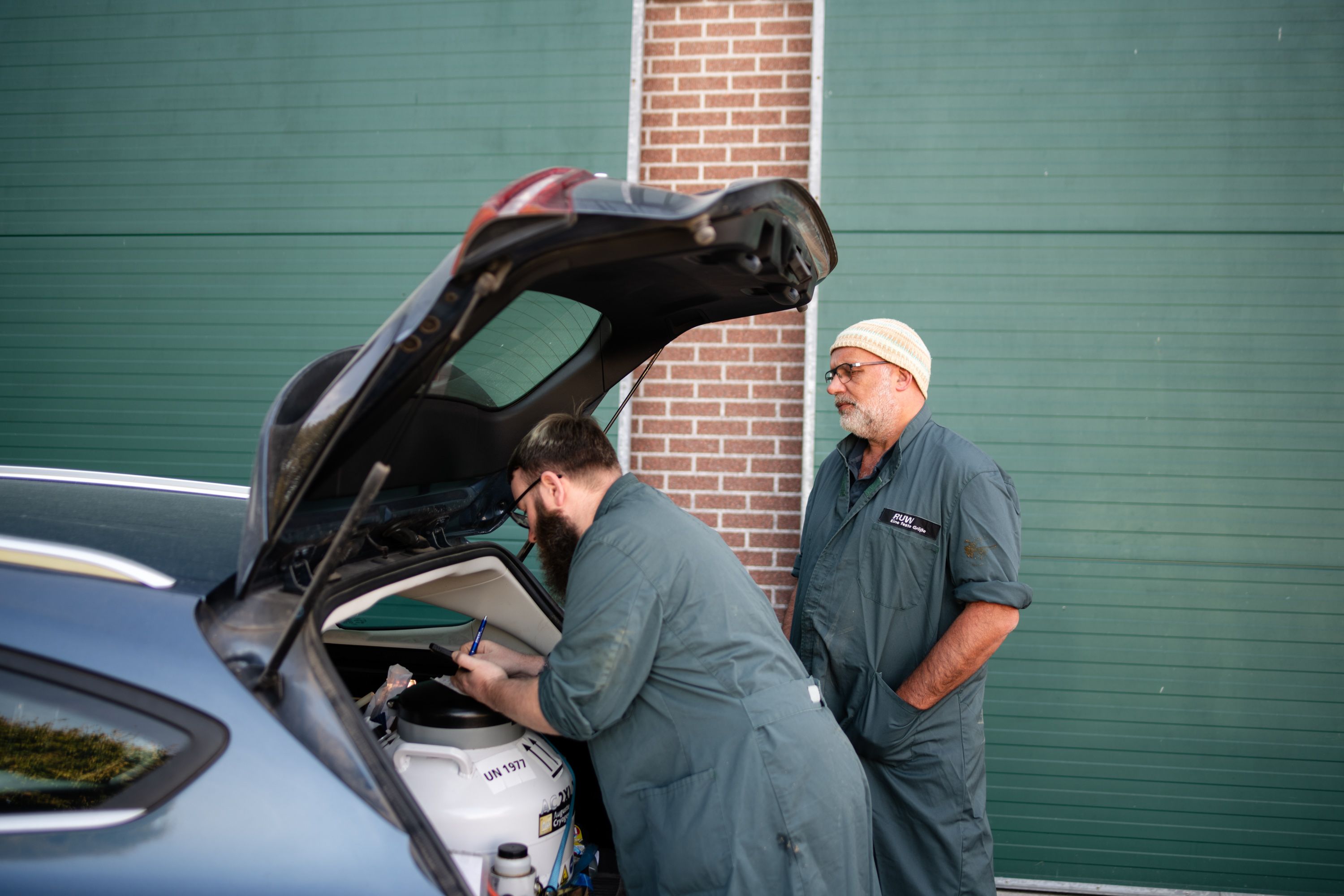 Vor einem offenen Kofferaum stehen zwei Männer in Arbeitskleidung. Sie holen Materialien aus dem Auto für die Besamung von Kühen.