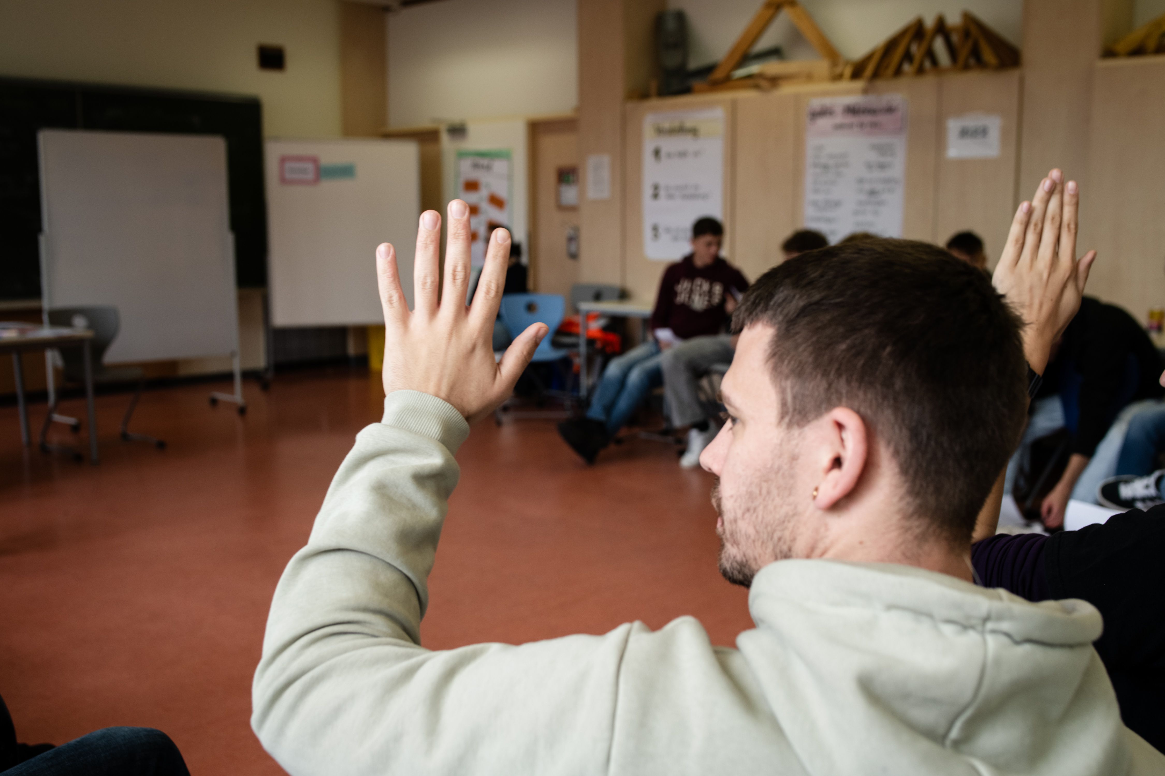 Bildausschnitt einer Berufsschulklasse, ein Schüler im vorderen Bildbereich meldet sich.